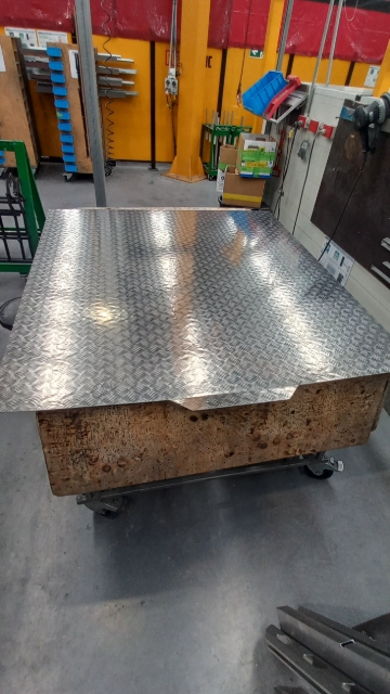 <p>Take lid shell from trolley &amp; place it tread side down on table.</p><blockquote><p>Ensure both sides of lid shell overhang the table enough to fit extrusion. Make sure you are working on a clean table to avoid scratches</p></blockquote><p></p>