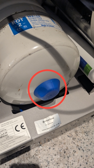<ol><li><p>Remove the cover from the unit and gently lay the unit over, exposing the bottom of the storage tank.</p></li><li><p>Remove the blue cover</p></li></ol><p></p>