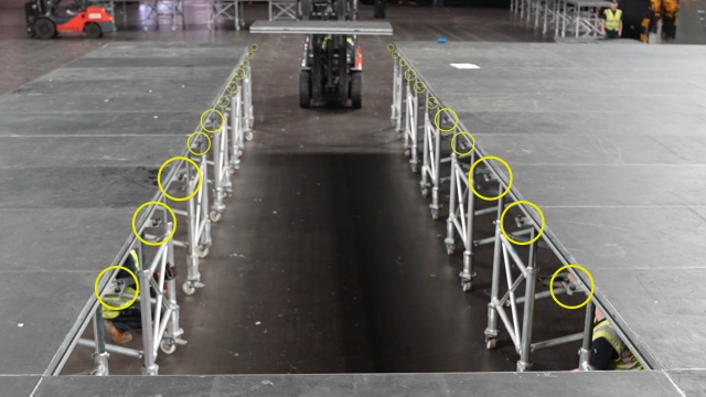 <h1>Adjust Corner Pieces</h1><p></p><p></p><p>On the edges where a bridge panel will be placed.</p><p></p><p>For each corner piece:</p><ul><li><p>One person lift the stage panel.</p></li><li><p>One person rotate the corner piece so that two studs are sticking out toward the gap where a bridge panel will be placed.</p></li></ul><p></p><p></p>